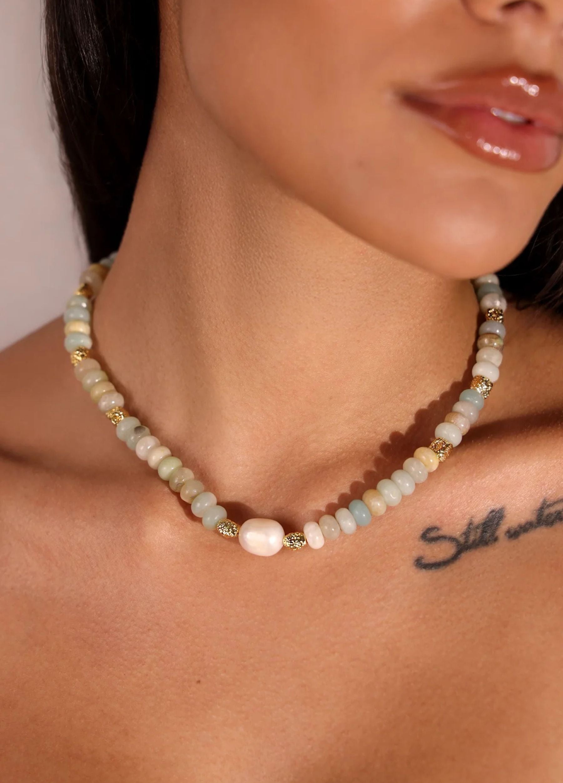 Necklace with beads and pearls worn by a person, with a tattoo visible on the shoulder.