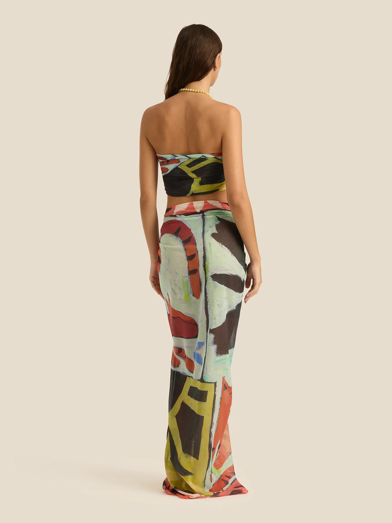 Woman wearing a strapless, long, multicolored dress with abstract patterns on a beige background
