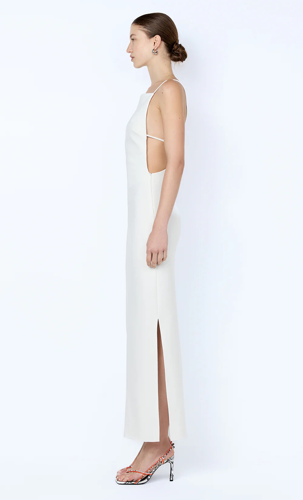 Woman wearing a white dress with thin straps and a slit on a white background