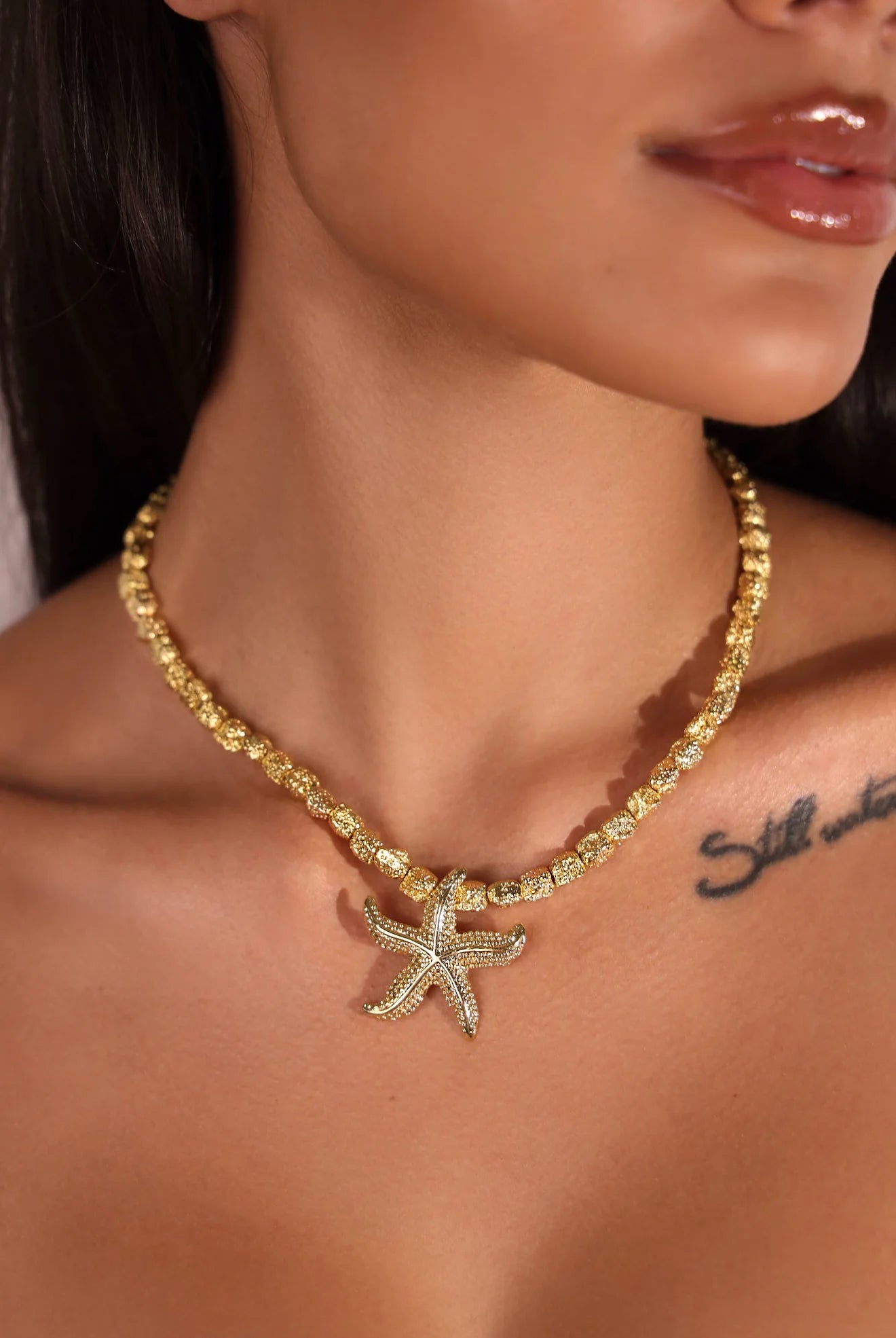Gold necklace with a starfish pendant worn by a person
