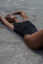 Person lying on a sandy beach with water reflecting sunlight