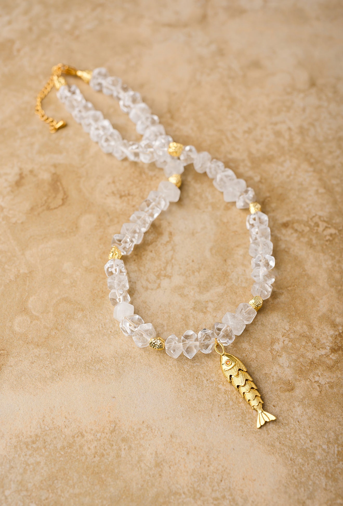 Necklace with clear beads and gold fish charm on a beige background