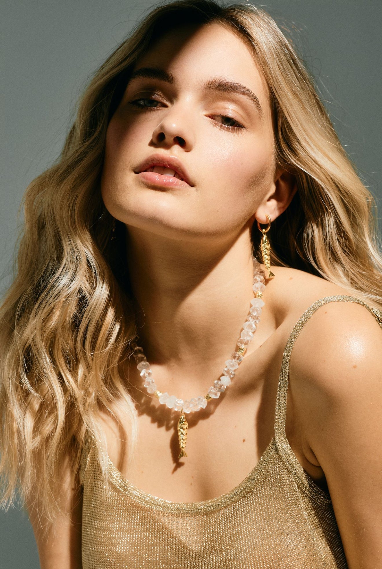 Woman wearing a gold tank top and pearl necklace against a neutral background