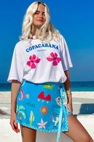Woman wearing a 'Copacabana' t-shirt and colorful skirt on a beach.
