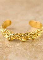 Gold bracelet with intricate design on a beige background