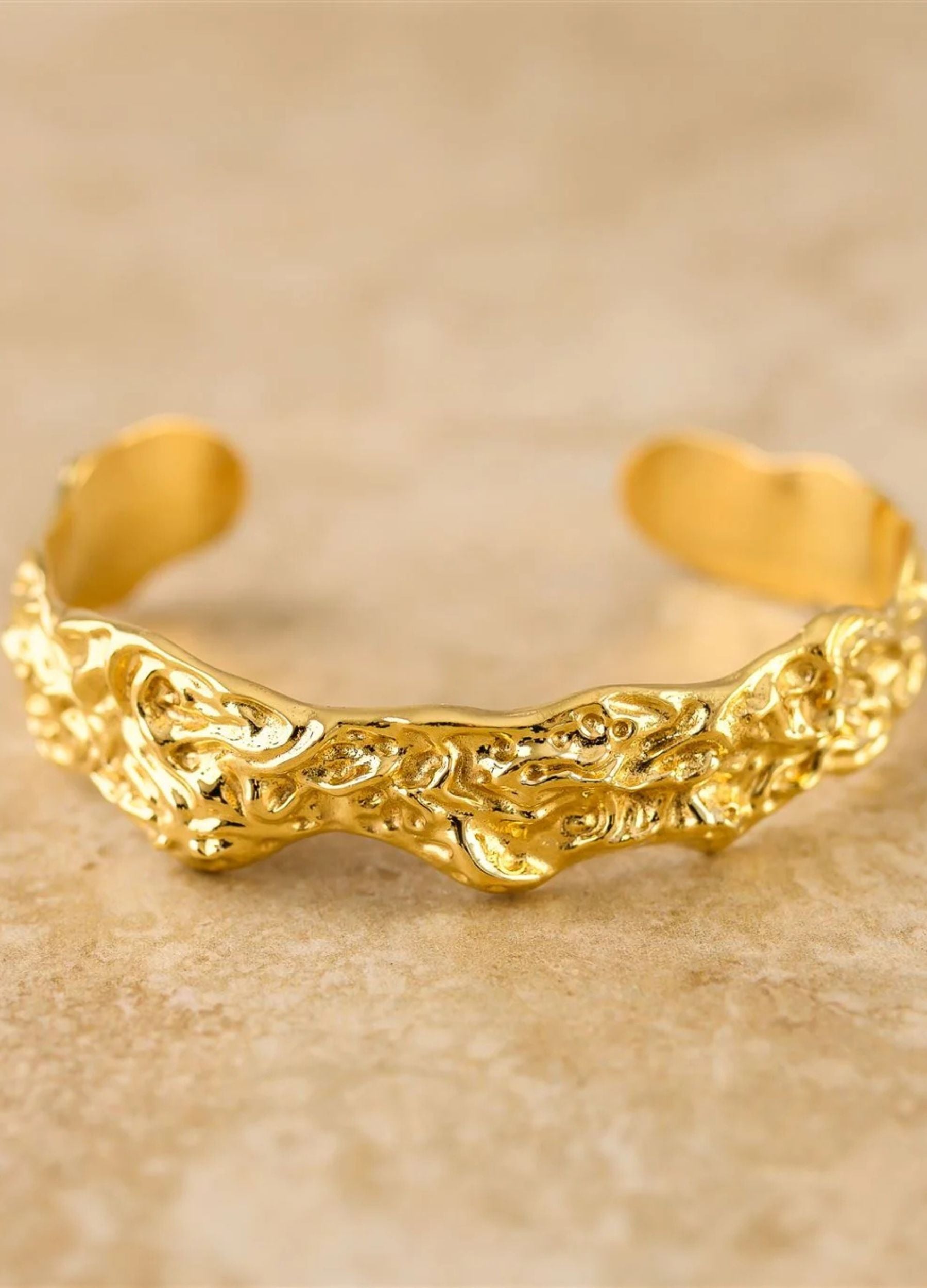 Gold bracelet with intricate design on a beige background