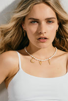 Woman wearing a pearl necklace with charms against a neutral background
