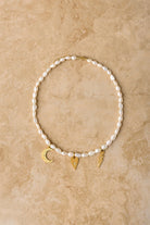 Pearl necklace with gold charms on a beige stone surface
