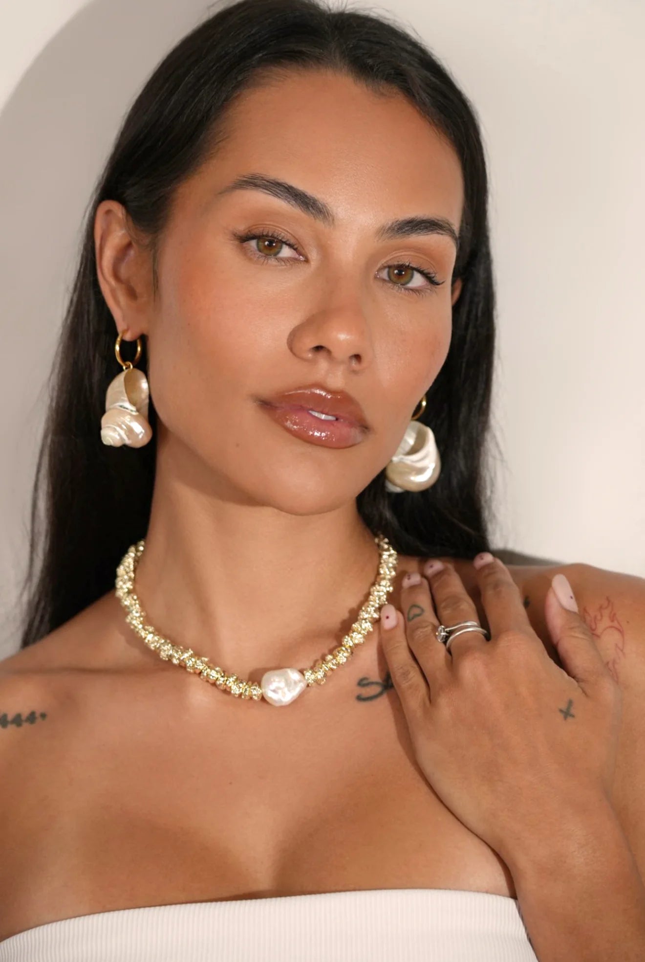 Woman wearing a gold necklace and pearl earrings with a neutral background