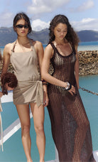 Two women in swimsuits standing on a beach with mountains in the background