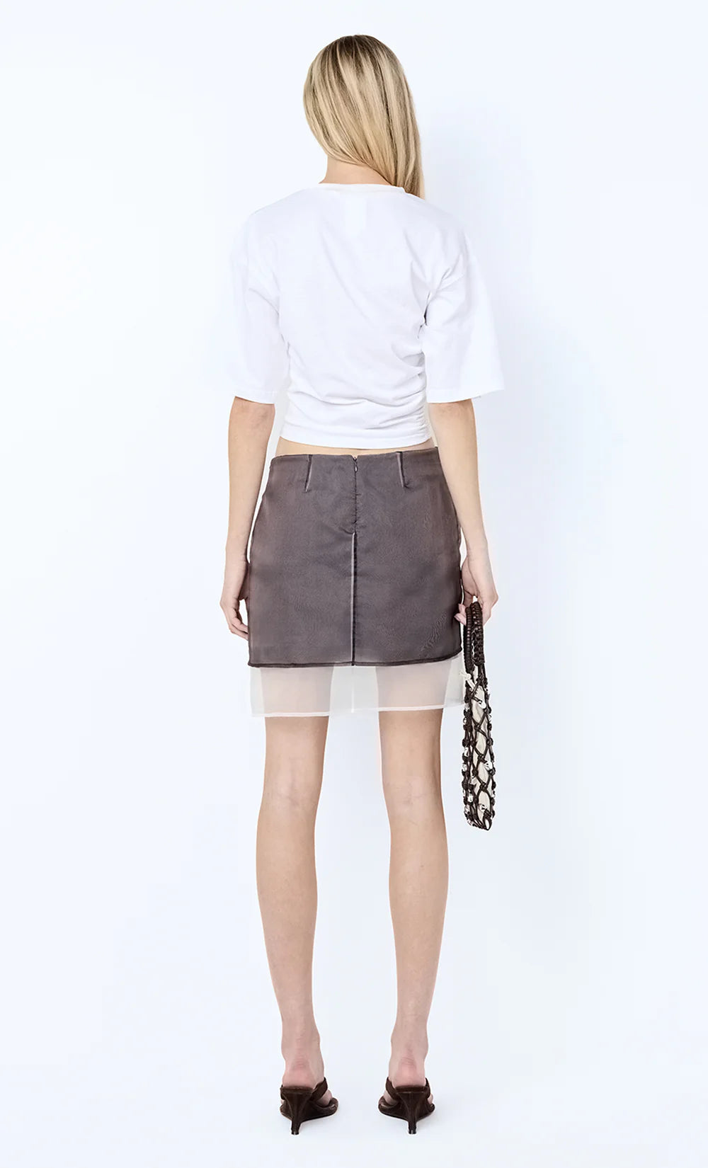 Person wearing a white top and gray skirt with sheer overlay on a white background