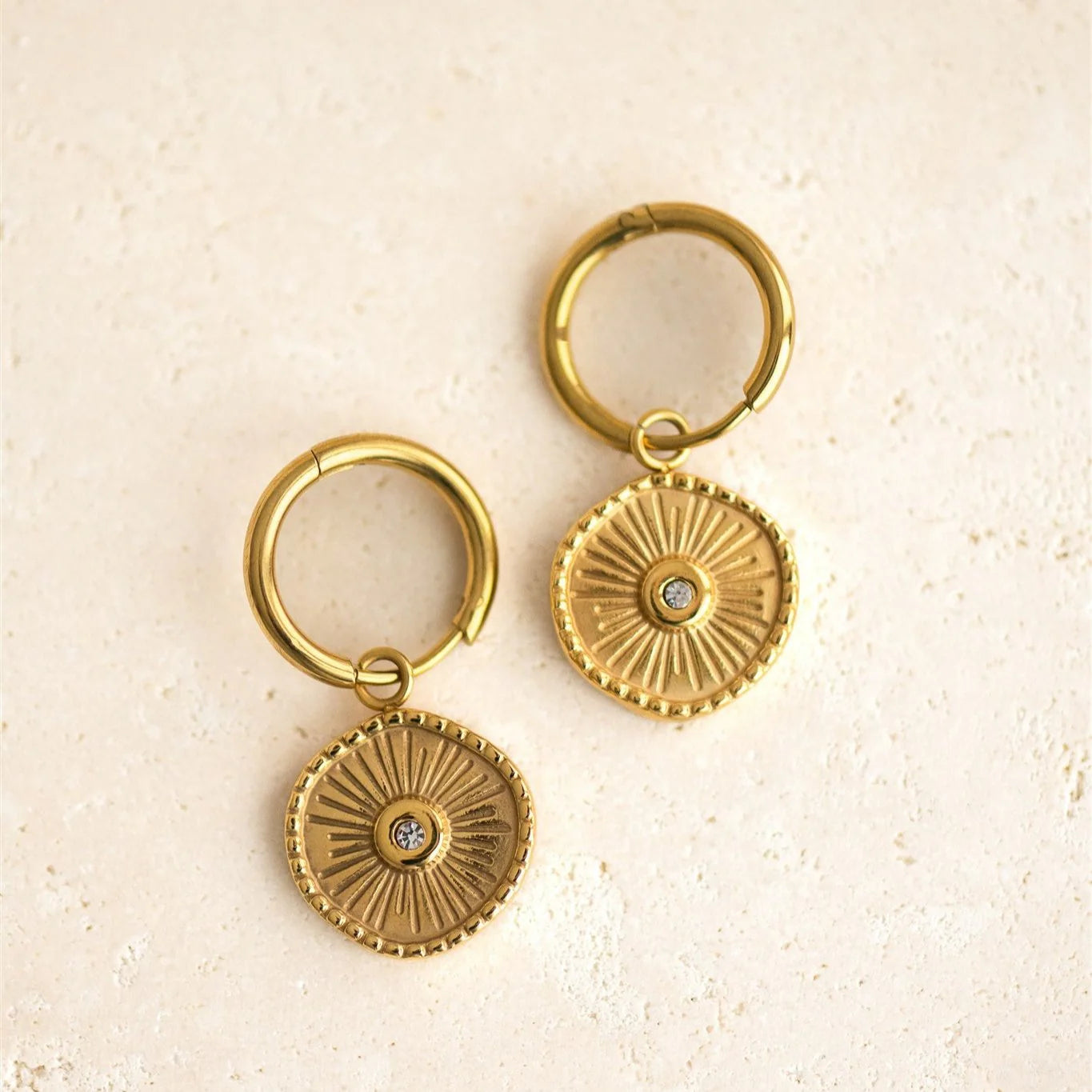 Pair of gold hoop earrings with circular designs on a beige background