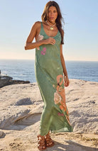 Woman in a green floral dress standing on a beach with ocean in the background
