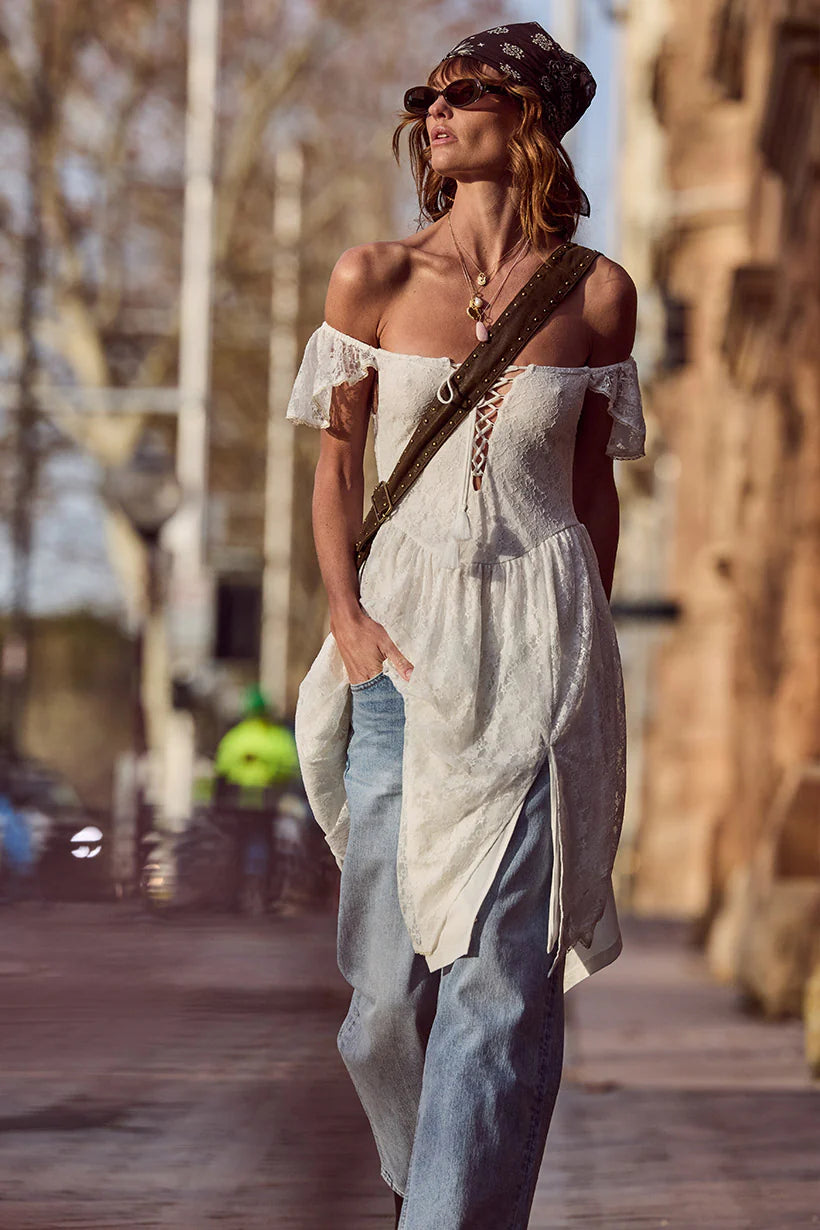 Woman in a white off-shoulder dress and blue jeans walking outdoors.