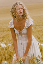 Woman in a white dress sitting in a field of tall grass and wildflowers