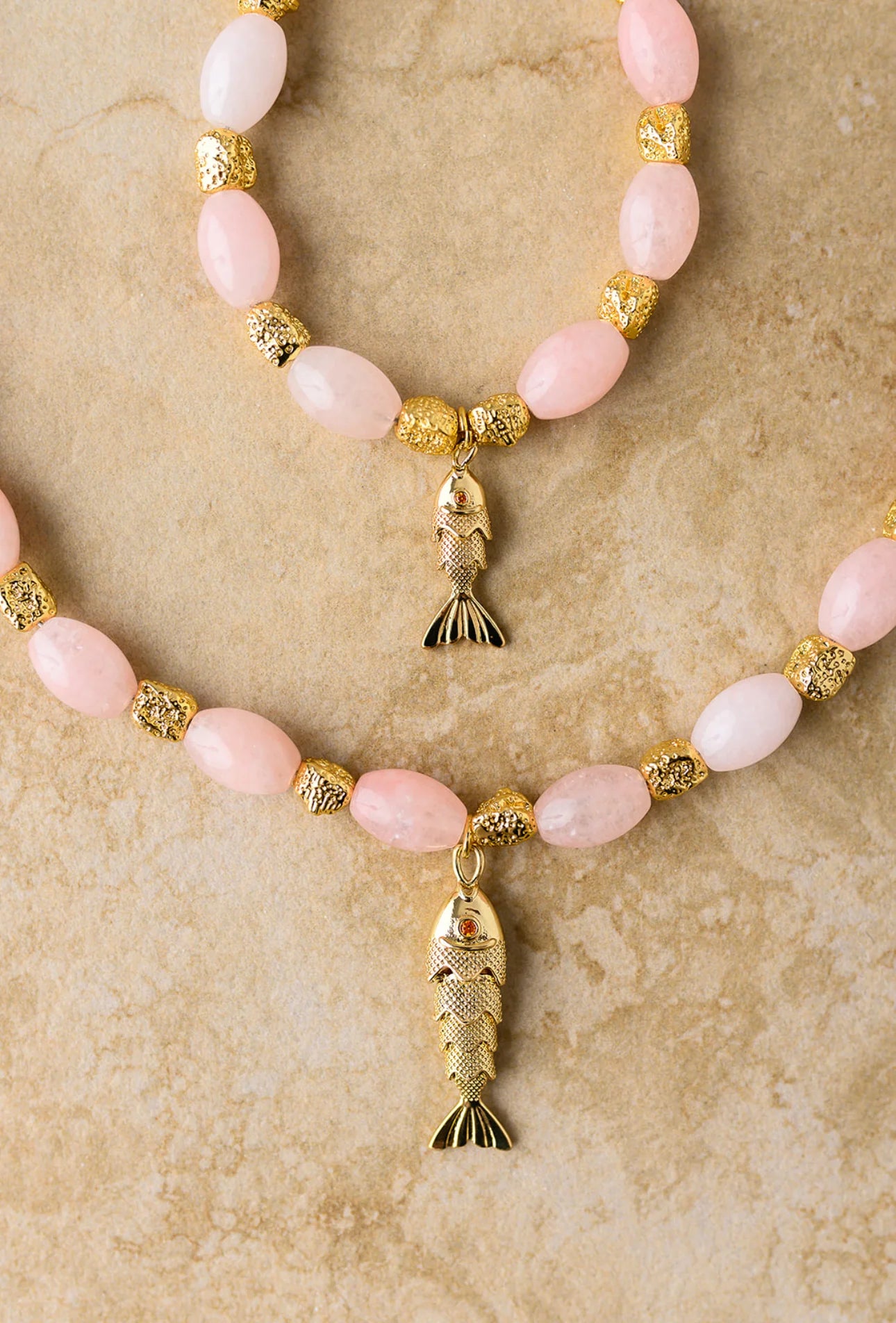 Necklace with pink beads and gold fish pendants on a beige background