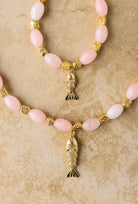 Necklace with pink beads and gold fish pendants on a beige background