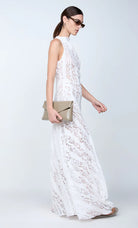 Woman in a white lace dress holding a beige clutch against a white background