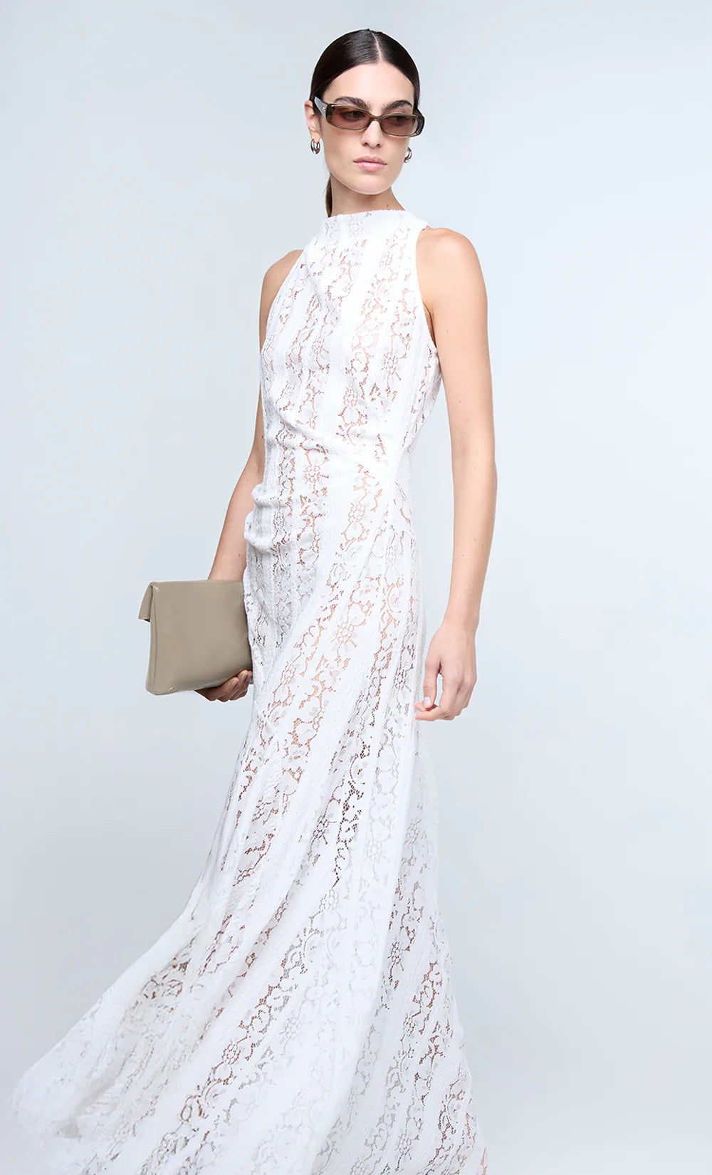 Woman wearing a white lace dress holding a clutch against a light gray background