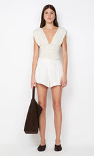 Woman wearing a white sleeveless dress holding a brown bag on a white background