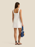 Woman wearing a white dress holding a blue bag on a beige background