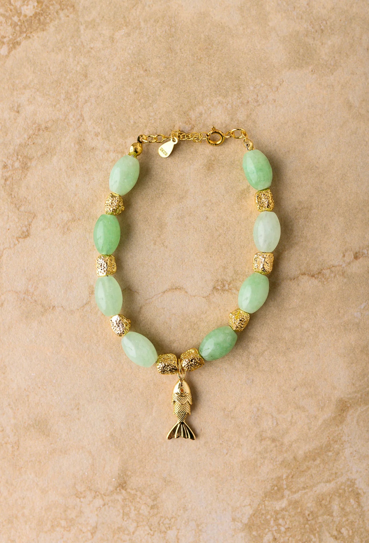 Bracelet with green beads and gold accents on a beige background
