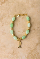 Bracelet with green beads and gold accents on a beige background