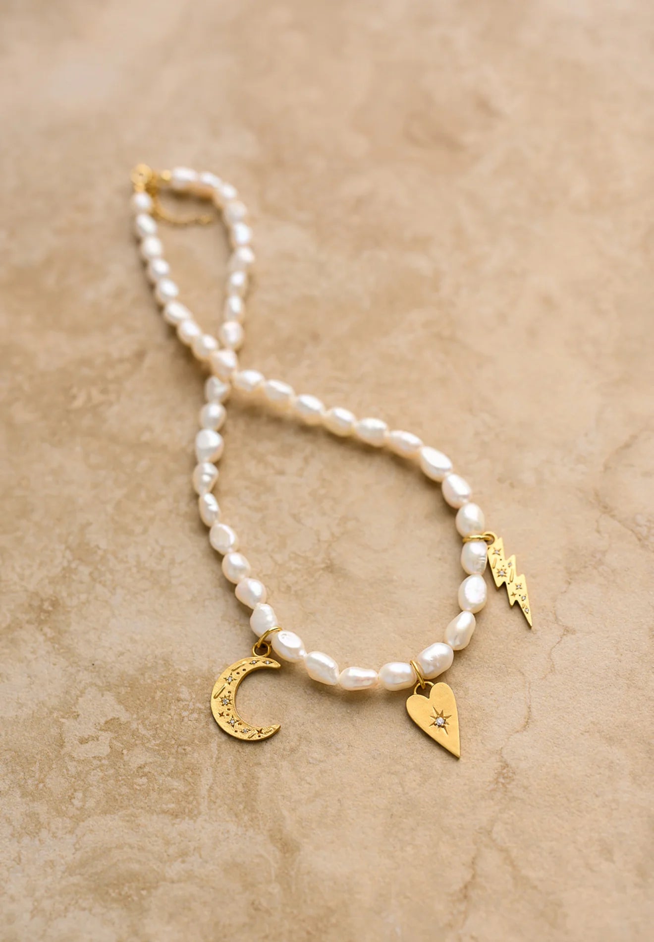 Pearl bracelet with gold charms on a beige background