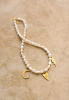 Pearl bracelet with gold charms on a beige background