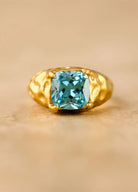 Gold ring with a blue gemstone on a beige background