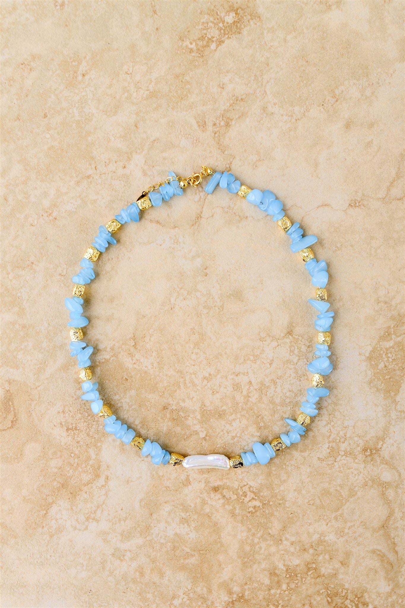 Necklace with blue and gold beads on a beige marble background