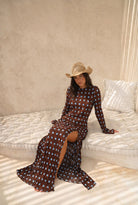 Woman in a patterned dress and straw hat sitting on a white couch.