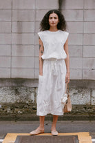 Woman wearing a white outfit standing against a textured wall.