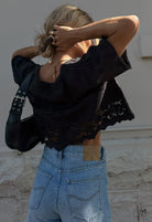 Person wearing a black lace top and blue jeans against a stone wall.