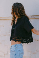 Person wearing a black lace top and blue jeans against a light-colored wall.