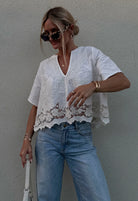 Woman wearing a white lace top and blue jeans against a gray wall