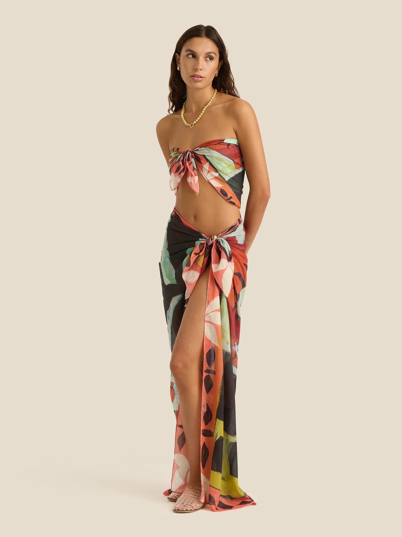 Woman wearing a floral one-shoulder top and long skirt on a beige background