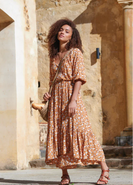 Woman in a floral dress standing in front of a stone wall.