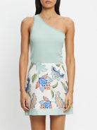 Woman wearing a light green one-shoulder top and floral skirt against a white background