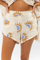 Beige shorts with sun and moon pattern worn by a person on a white background