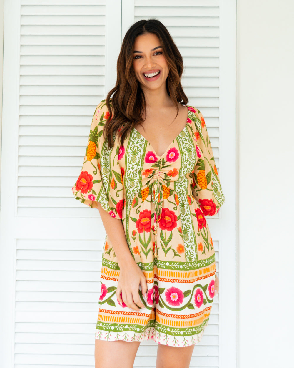 Woman wearing a colorful floral dress standing in front of white blinds.