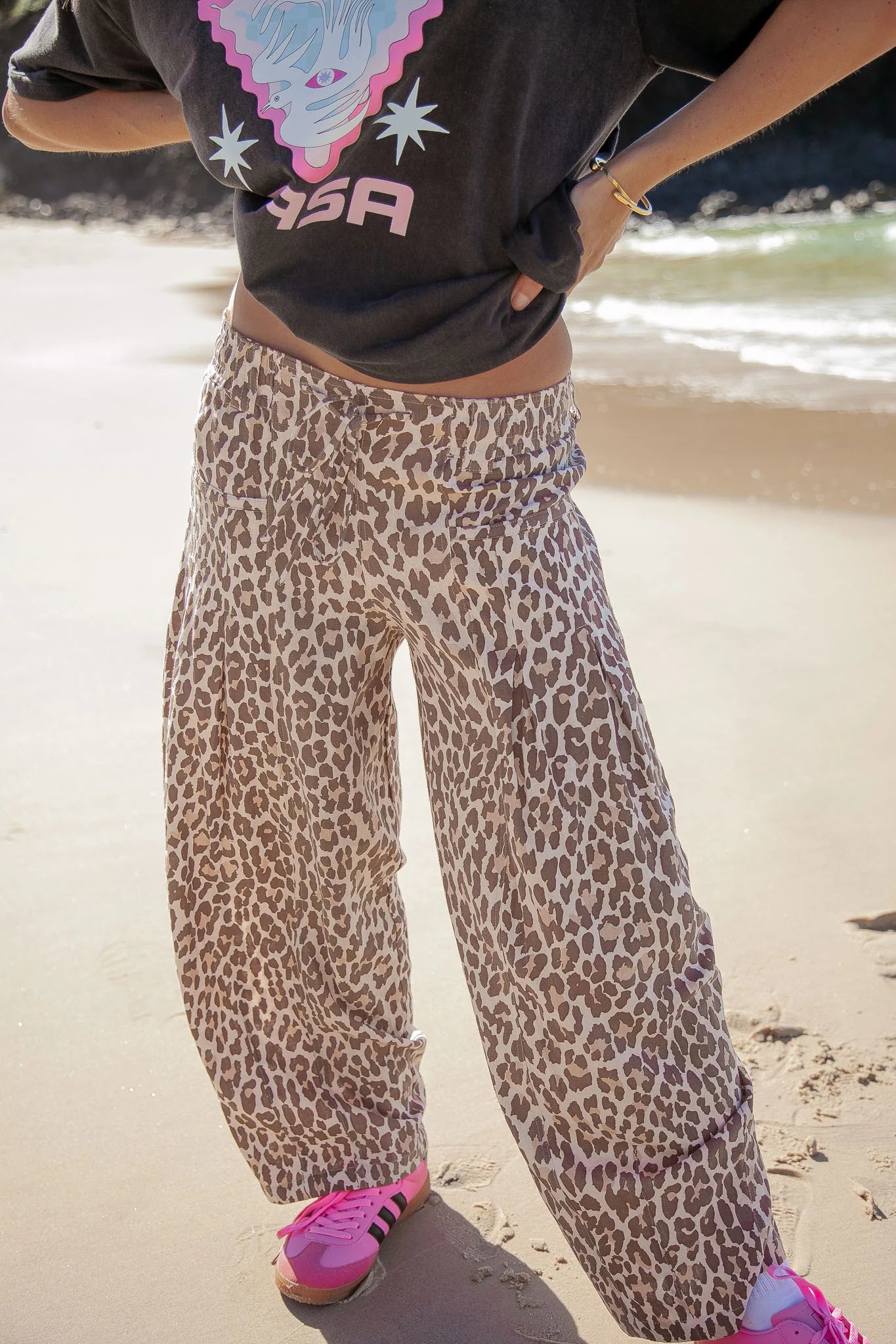 Person wearing leopard print pants and a black top with 'RCA' logo on a beach.