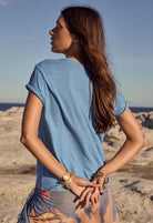Woman in a blue shirt standing on a rocky beach with a clear sky.