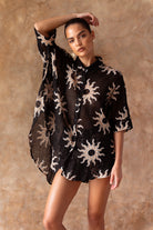 Woman wearing a black dress with sun patterns against a beige background