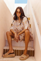 Woman sitting on a step wearing sunglasses and a floral dress.