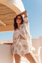 Woman in a patterned outfit standing under a sunshade with a clear blue sky.