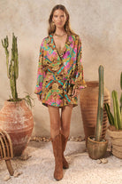 Woman in a colorful patterned dress standing among potted plants and rustic decor.