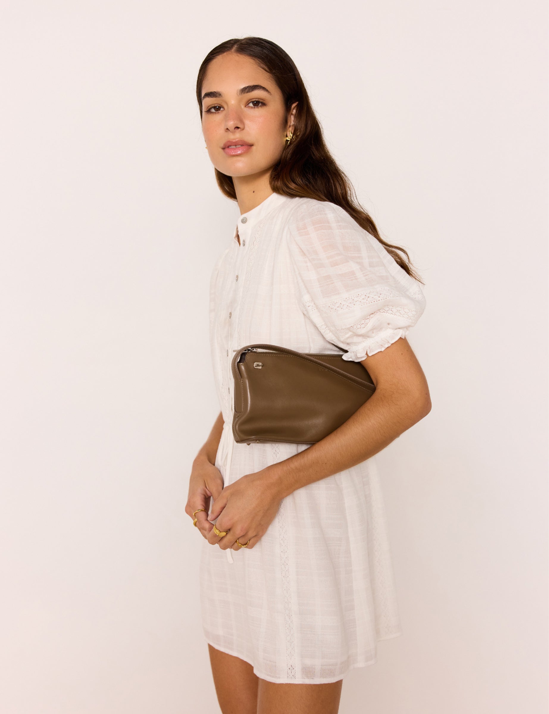 Woman holding a brown leather clutch against a plain background