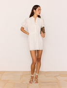 Woman wearing a white dress holding a clutch against a plain background