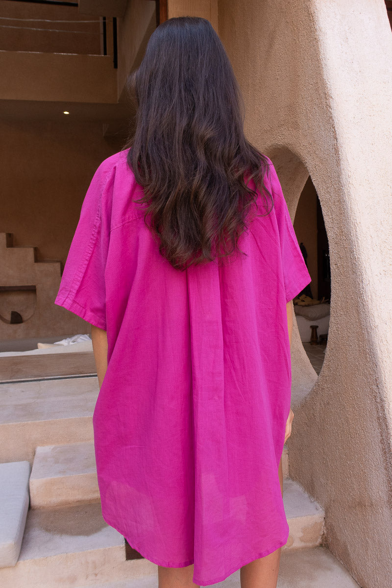 Person wearing a bright pink shirt standing in front of a textured wall.